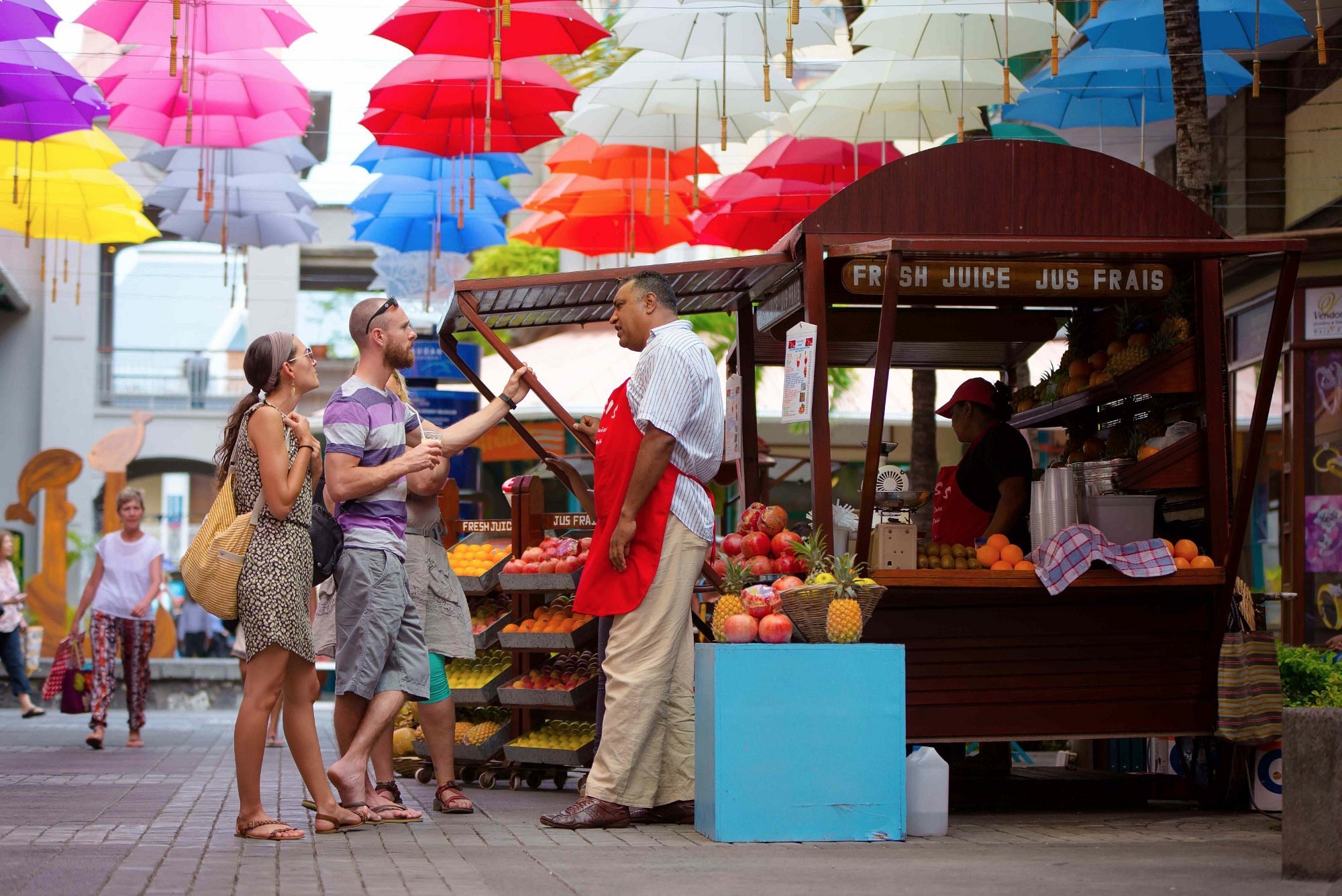 Tourists at a fresh juice stall under the colourful umbrellas at Caudan Waterfront, Port Louis